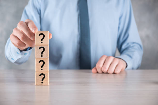 istock Businessman hold and put wooden cube block shape with question marks on grey table. Space for text.concept for confusion, question or solution 1340437276