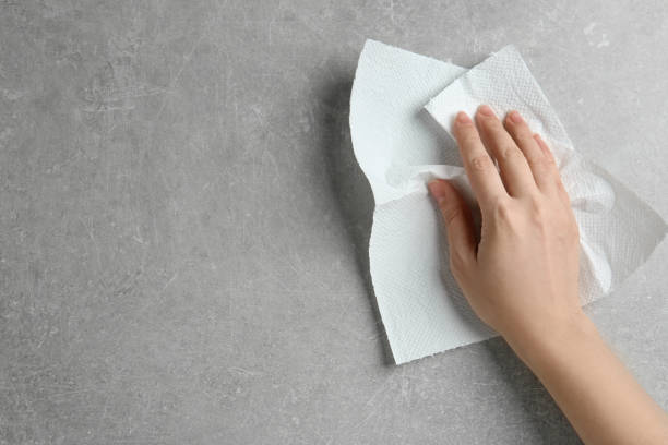istock Woman wiping light grey stone table with paper towel, top view. Space for text 1340439378