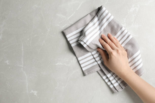 istock Woman wiping light grey marble table with kitchen towel, top view. Space for text 1340439604