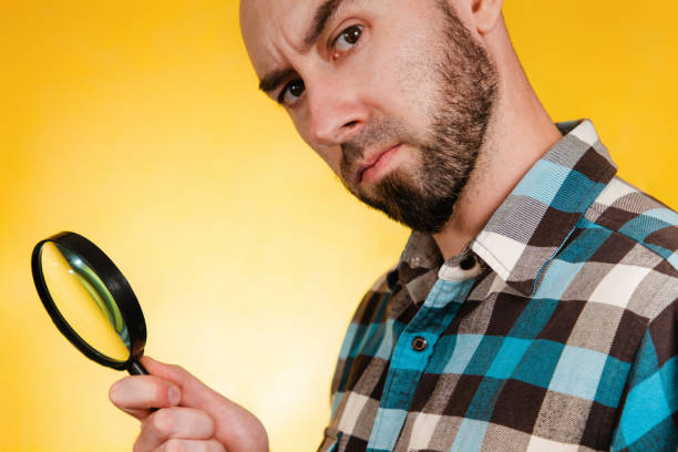 istock The concept of finding and solving problems. A bald man with a beard, dressed in a blue plaid shirt, holding a magnifying glass and looking intently. Copy space 1340440358