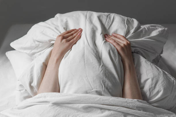 mujer en la cama escondiendo la cara debajo de la almohada - debajo de fotografías e imágenes de stock