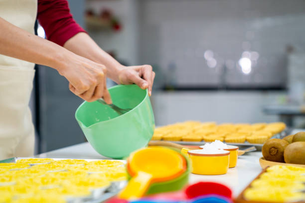Asian woman bakery shop owner preparing bakery in the kitchen. Adult female making whipping cream cheese from fresh milk on the table. Small business entrepreneur and indoor activity lifestyle baking concept.