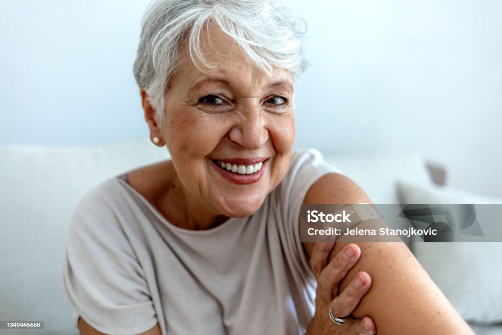 Elderly lady getting immunization via anti-viral vaccine. Proud mature woman smile after vaccination with bandage on arm. Beautiful smiling senior woman 70s after receiving the coronavirus vaccine. Elderly lady getting immunization via anti-viral vaccine. Vaccination Stock Photo