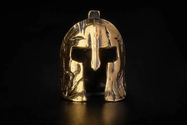 A figurine. Golden Spartan helmet. Metal on a black background. Headgear and equipment of soldiers