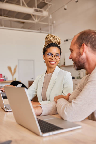 istock Two diverse businesspeople talking while working on laptops in an office 1340448594
