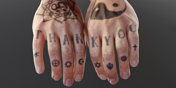 A shallow depth of field image of two hands close together heavily tattooed with both religious symbols from various major religions and the words 'THANK YOU' on the fingers. Shot against a plain background with shallow depth of field.