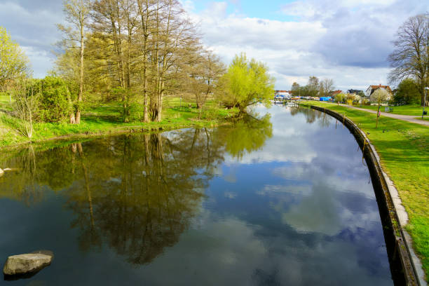 Narrowboat travelling along English rural countryside scenery on British waterway canal with blue sky in autumn fall season past moored boats