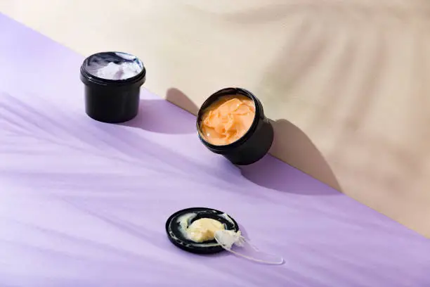 Natural products for body and face skin care. Orange cream in black jar on purple and beige background