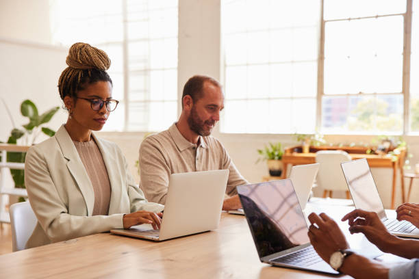 istock Diverse businesspeople working on laptops while sitting at a table in an office 1340452134