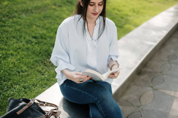 istock Young woman reading a book outdoors 1340452892