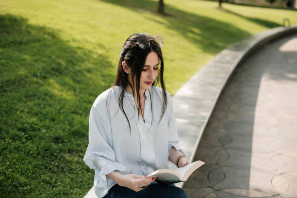 istock Young woman reading a book outdoors 1340452914