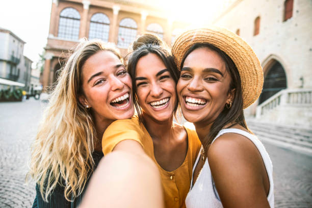 three young women taking selfie portrait on city street - multicultural female friends having fun on vacation hanging outdoor - friendship and happy lifestyle concept - meisjes stockfoto's en -beelden