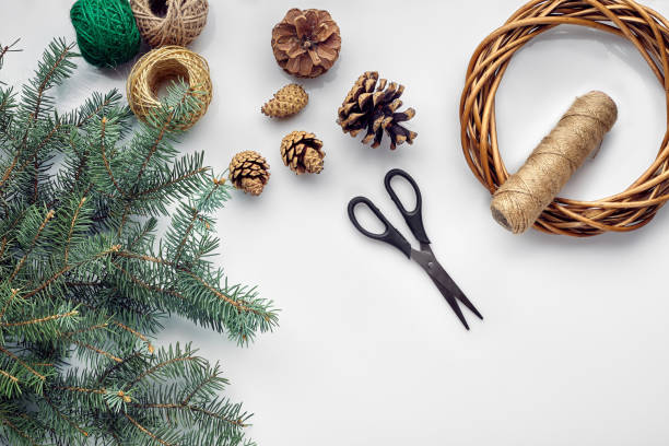 istock Beautiful festive handmade wreath base with three bumps near it, threads and twigs blue Christmas tree on the white table background, flat lay 1340455356