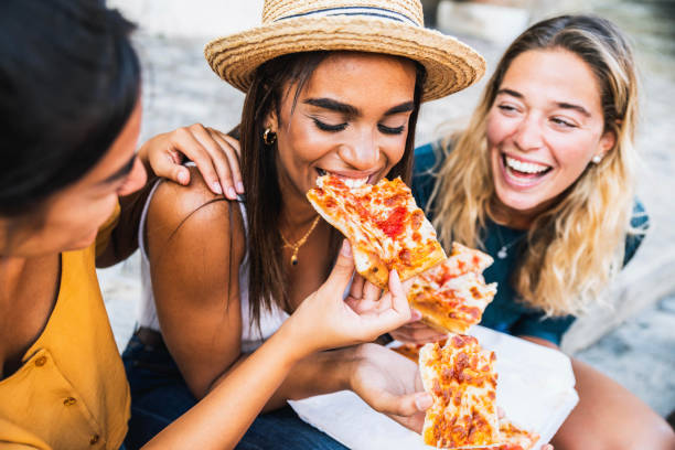 tre giovani amiche sedute all'aperto e mangiano pizza - donne felici che si divertono a godersi una giornata in città - concetto di stile di vita felice - teenager city life laughing group of people foto e immagini stock