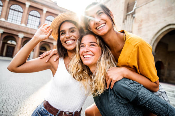 Three young diverse women having fun on city street outdoors - Multicultural female friends enjoying a holiday day out together - Happy lifestyle, youth and young females concept stock photo