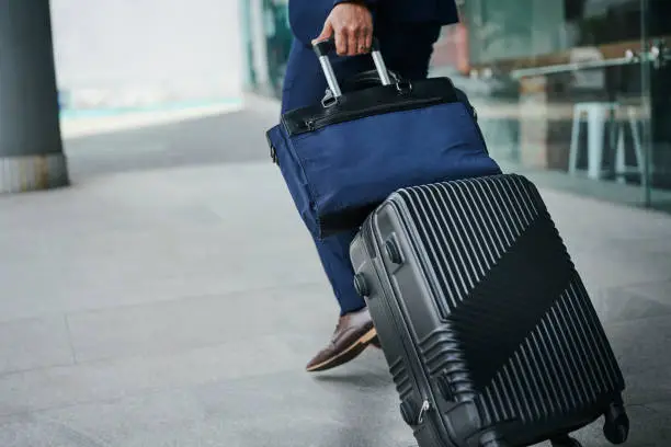Close-up of a businessman pulling a rolling suitcase and bag along a sidewalk outside before a business trip