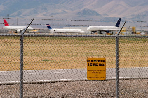 Aircraft lining up for takeoff behind barbed wire fence and no trespassing sign.