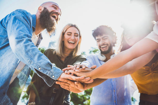 Multiracial happy young people stacking hands on top of each other - Diverse friends unity togetherness in volunteer community - Concept about college, relationship, youth and human resources stock photo