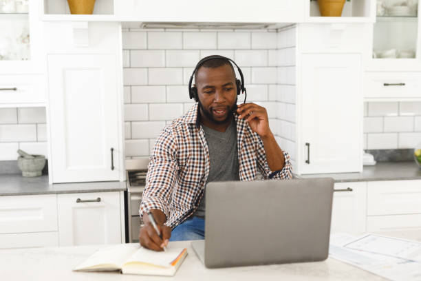 istock African american man sitting in kitchen making video call using laptop and headset 1340459369