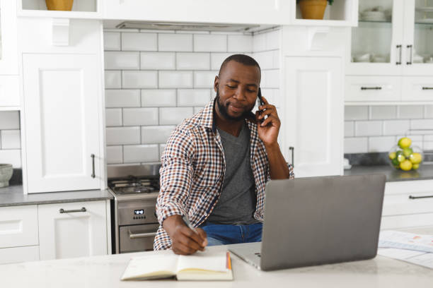 istock African american man sitting in kitchen working using laptop and smartphone 1340459546