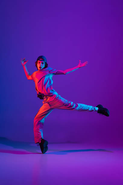 istock Young stylish man, break dancing, hip-hop dancer practicing solo in casual clothes isolated over purple background in neon pink light at dance hall 1340462906