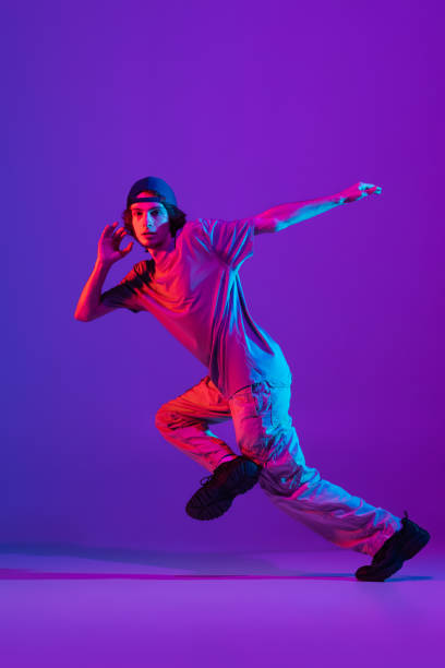 istock Young stylish man, break dancing, hip-hop dancer practicing solo in casual clothes isolated over purple background in neon pink light at dance hall 1340462932