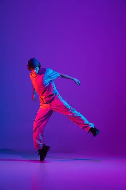 istock Young stylish man, break dancing, hip-hop dancer practicing solo in casual clothes isolated over purple background in neon pink light at dance hall 1340462935