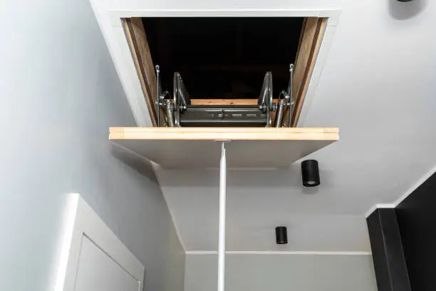 Photo of Folding metal stairs to the attic in the ceiling, closed hatch with a tube for opening, modern look.