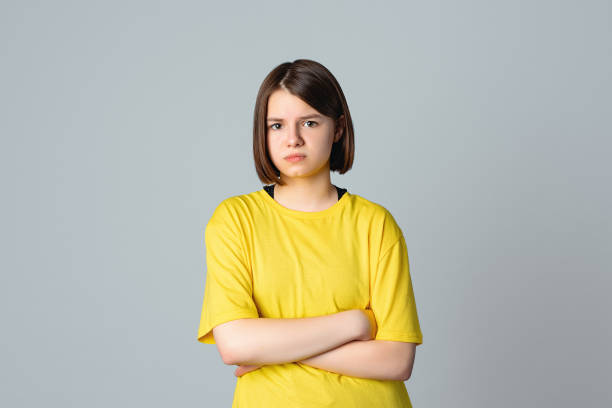 Portrait of a offended teen girl with crossed arms, standing over light grey background. Teen disappointment. Loneliness boredom Portrait of a offended teen girl in yellow casual t shirt with crossed arms, standing over light grey background. Disobedience problem. Depressed young girl. Teen disappointment. Loneliness boredom 12 13 years stock pictures, royalty-free photos & images
