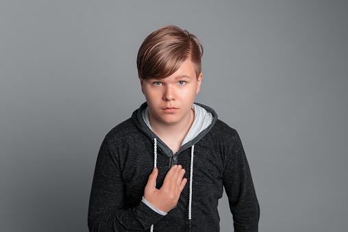 Confused Teen boy pointing displeased and frustrated to the himself hand, this is not me, stands over grey background, wearing in casual clothes