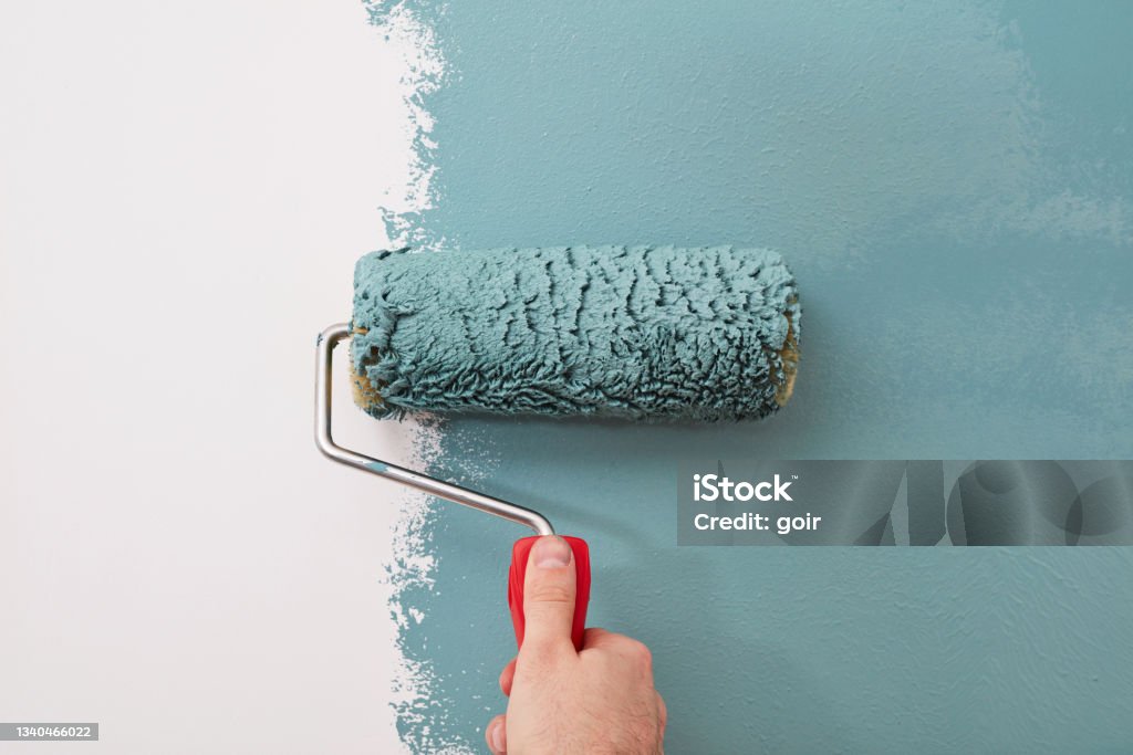 Close-up of a paint roller on the wall Male hand painting wall with paint roller Painting - Activity Stock Photo