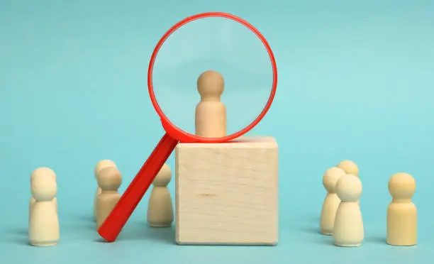 Photo of wooden figures of men stand on a beige background and a plastic magnifying glass