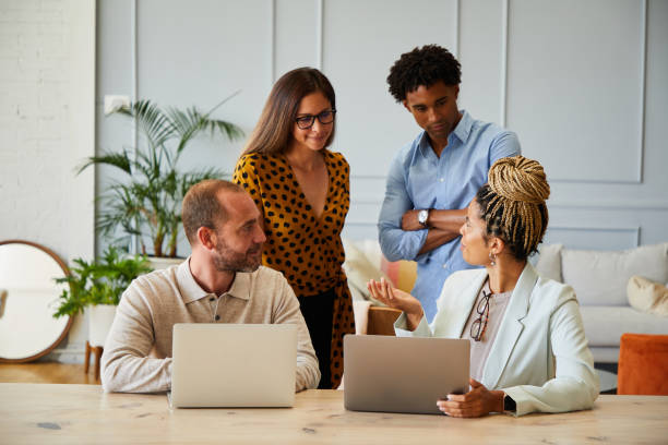 istock Businesspeople talking with colleagues while working on laptops in an office 1340470766