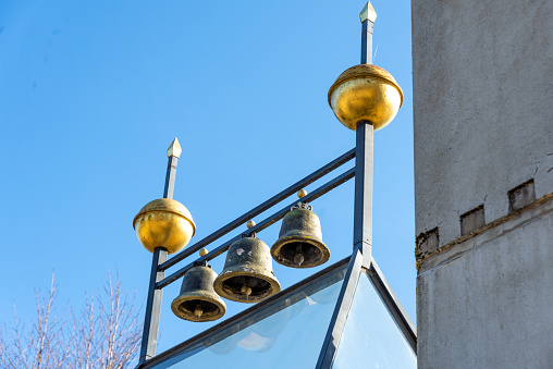 Three bells on a roof, mounted on a metal frame with gold colored balls as embellishment. Photographed against the sky.