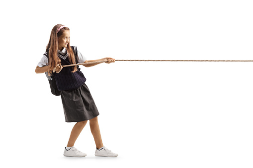 Full length profile shot of a schoolgirl pulling a rope isolated on white background