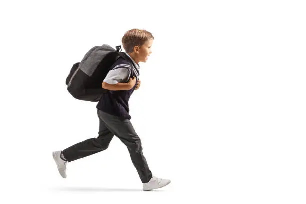 Full length profile shot of a schoolboy in a uniform running fast isolated on white background
