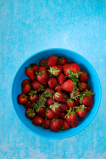Stock photo showing elevated view of blue dish full of fresh, bright red, whole strawberries on turquoise background. The strawberry is a popular summer fruit that is considered to be an especially healthy snack 'super food', since they are packed with beneficial antioxidants and fibre, being a good source of vitamin C.