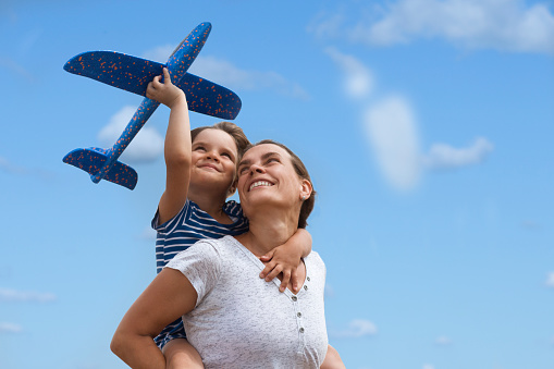 Happy family mom and child daughter playing together airplane against the background of the blue sea and sky. Leisure Travel Concept. summer time