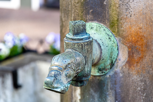 An old faucet that has no handle to open, but a square, which requires a tool. The tap is apparently made of copper, it is covered with verdigris.