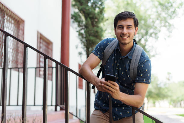 istock Happy male student holding phone and smiling at camera. 1340480653