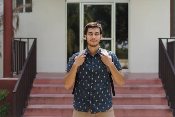 A university latin male student standing outside building and looking at the camera.