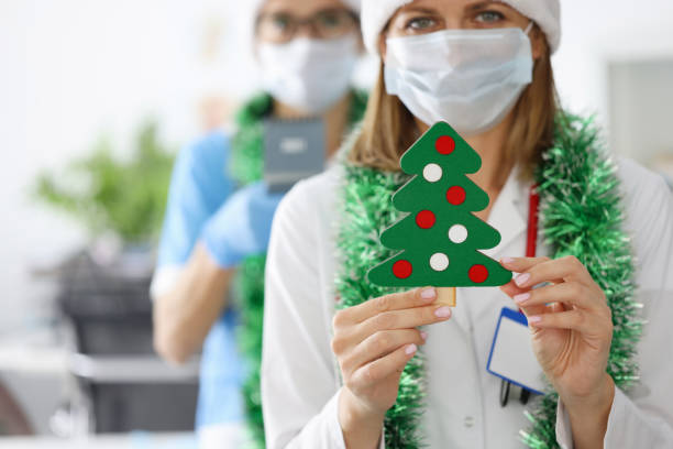 Doctors in santa hats and bright tinsel around their necks are holding toy christmas tree in clinic closeup stock photo