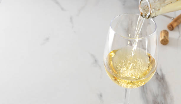 zbliżenie kieliszka do wina i proces nalewania białego wina, korkociągu i korka na stół z białego marmuru. puste miejsce - wine cork white wine grape zdjęcia i obrazy z banku zdjęć