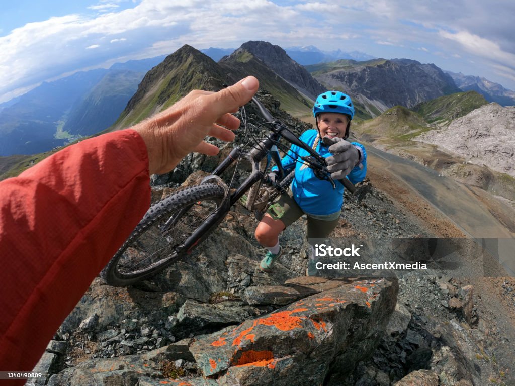 POV of female mountain biker hiking up mountain View past man's helping hand, in the European Alps Point of View Stock Photo