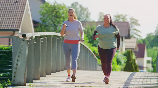 Two female friends talking and walking across a bridge with weights in their hands