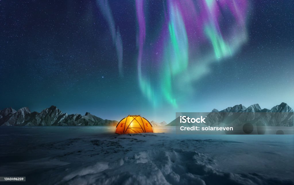 Camping Under The Northern Lights A tent pitched up in snow at night with the northern lights flickering in the sky above. Aurora Borealis and travelling. Photo composite. Aurora Borealis Stock Photo