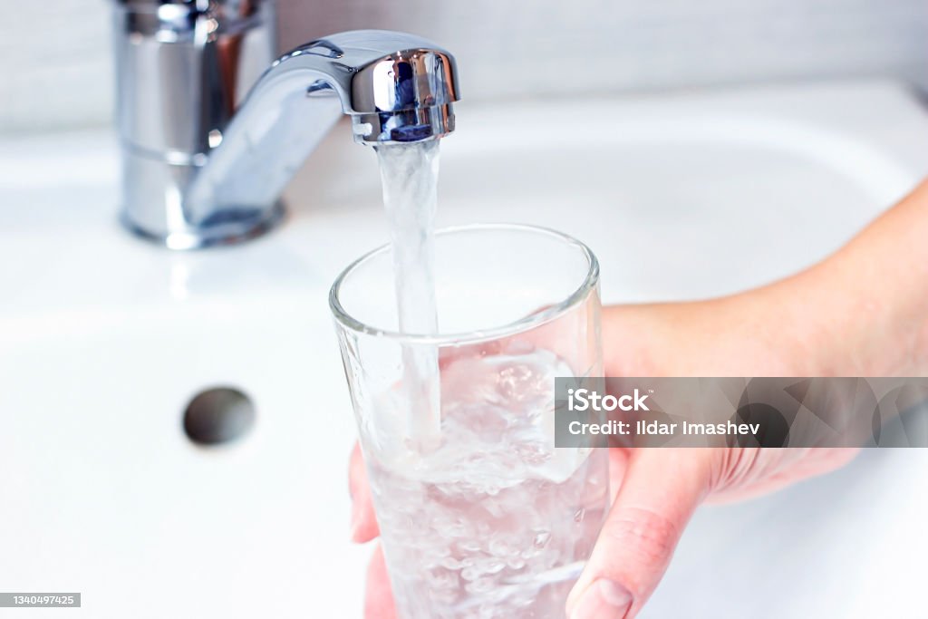 Young caucasian woman hand holding a glass with pure drinking water pouring from home faucet close up Young caucasian woman hand holding a glass with pure drinking water pouring from home faucet close up. Drinking Water Stock Photo