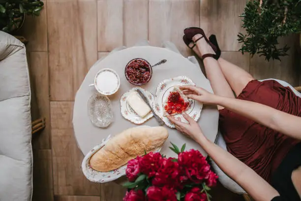 A high angle view of the elegant woman in high heels holding a slice of bread with raspberry jam on