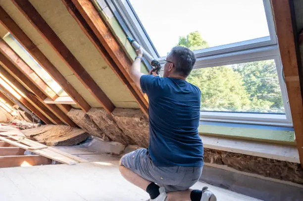 Photo of Craftsman caulking a new window in the attic.