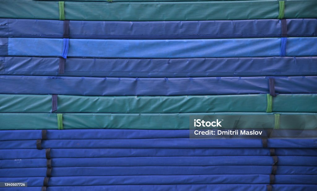 Mats of various thicknesses for acrobatics, folded in a high stack. Mats of various thicknesses for acrobatics, folded in a high stack. Blue, green and light blue mats with carrying handles. Gymnastics Stock Photo